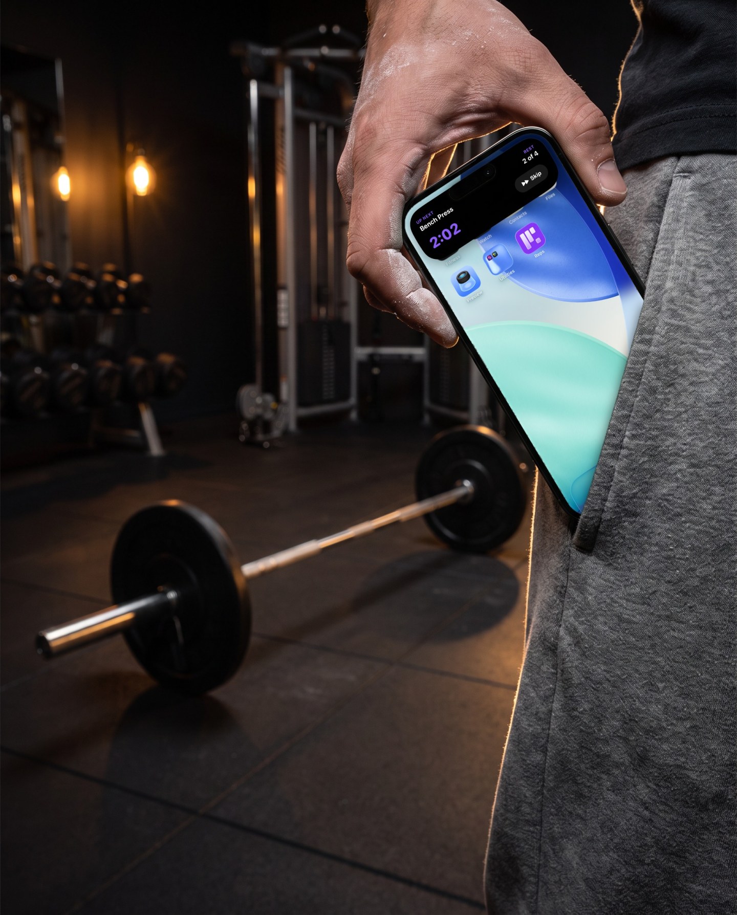 Between sets a chalked hand pulls the phone out of the pocket. The Reps rest timer runs in the Dynamic Island, bench press is next and about two minutes are left