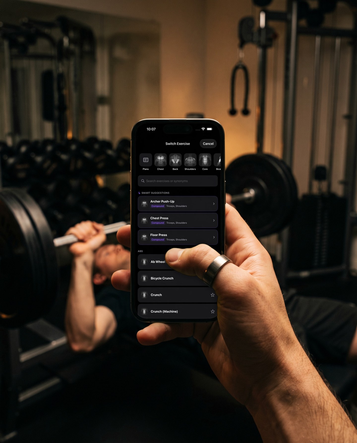 The bench is taken, so the phone shows Switch Exercise with smart suggestions for archer push ups, chest press and floor press, while someone else bench presses behind it
