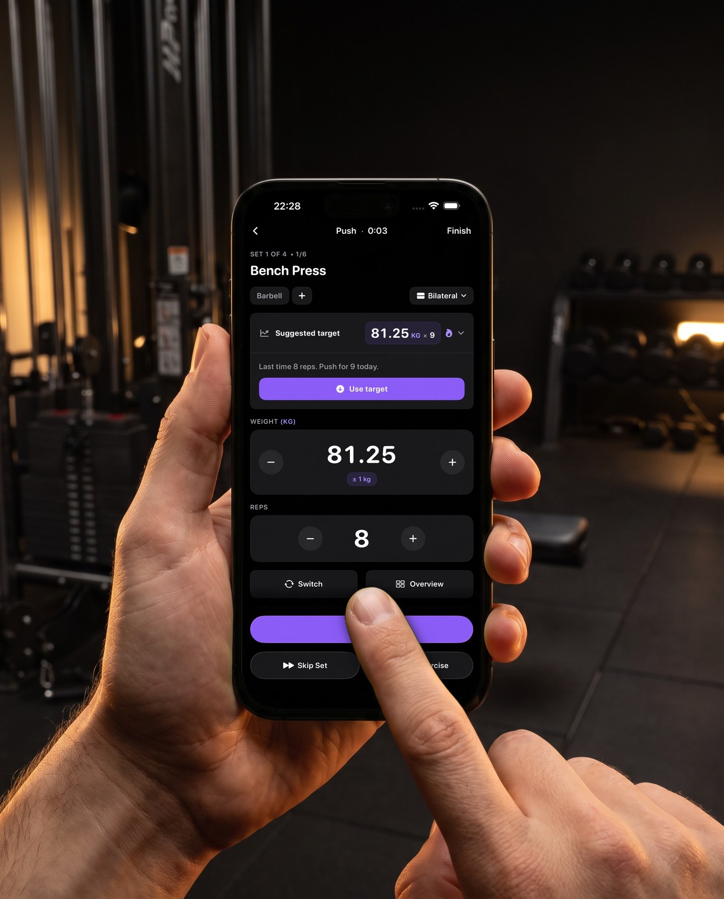 In a gym a finger taps the reps field on the Reps set screen showing bench press, suggested target 81.25 kilos for nine reps, last time eight reps