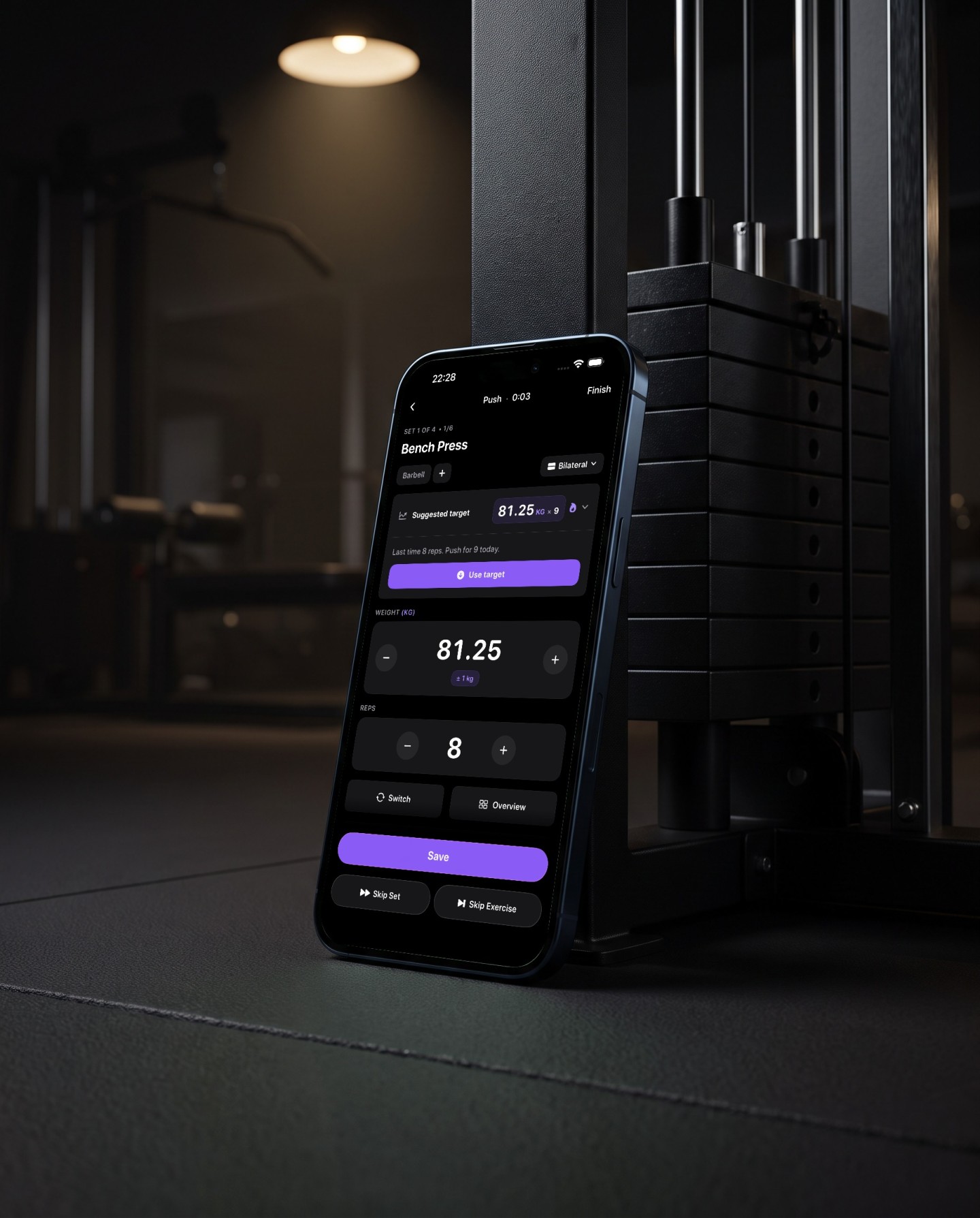 Reps set screen on a phone leaning against a cable machine weight stack showing bench press, suggested target 81.25 kilos for nine reps, last time eight reps